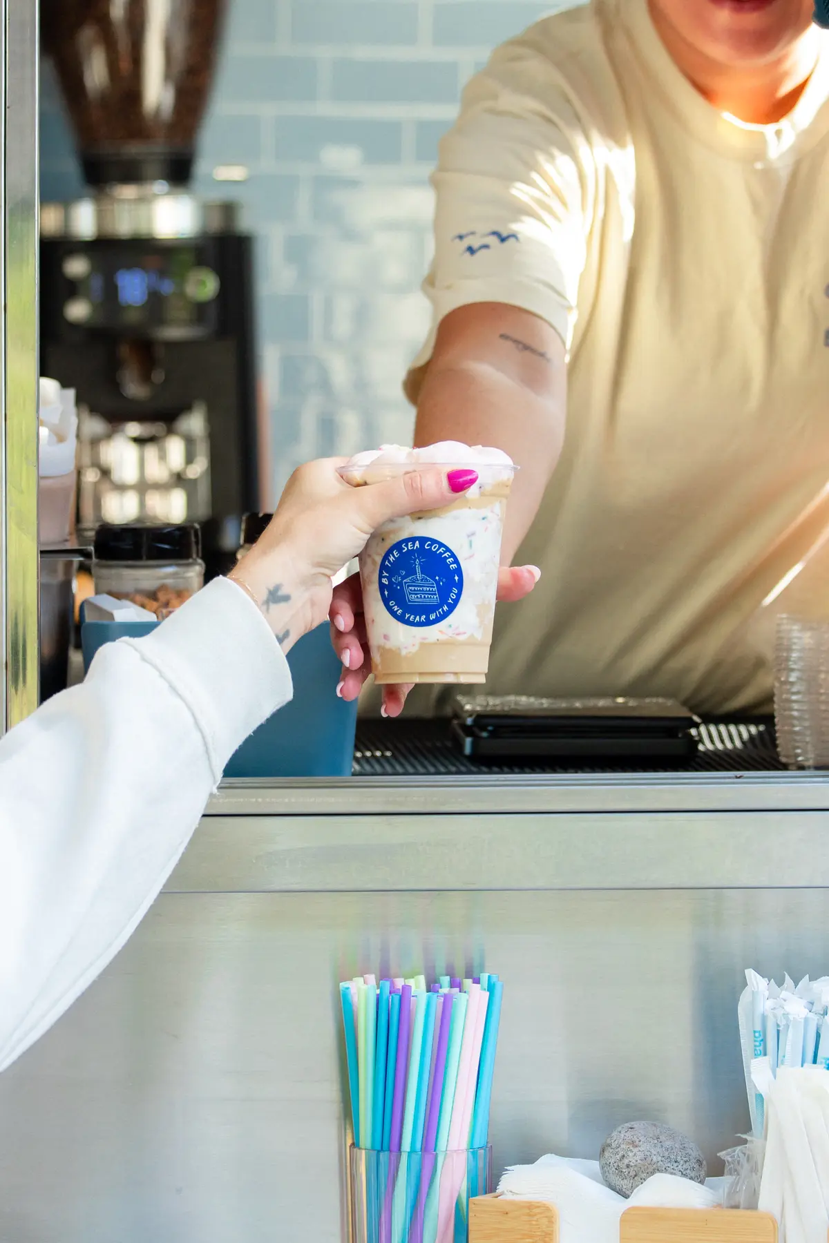 A By the Sea Coffee barista handing a branded iced coffee to a customer
